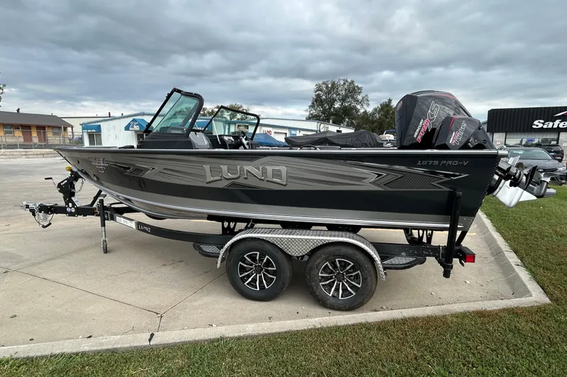 Slide: The Image of 2026 Lund 1875 Pro-V boat on trailer, parked outdoors under cloudy sky. - 1