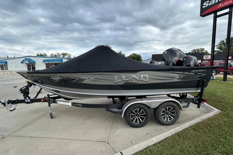 Slide: The Image of 2026 Lund 1875 Pro-V boat on trailer, covered, parked outdoors under cloudy sky. - 10