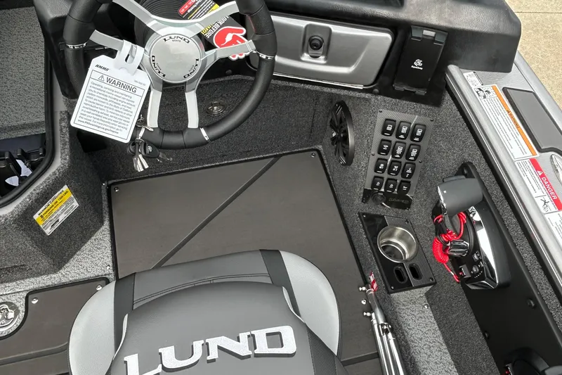 Slide: The Image of 2026 Lund 1875 Pro-V boat cockpit with steering wheel, control panel, and branded seat. - 16