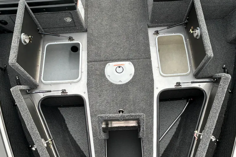Slide: The Image of 2026 Lund 1875 Pro-V boat interior storage compartments, featuring open hatches and carpeted surfaces. - 19
