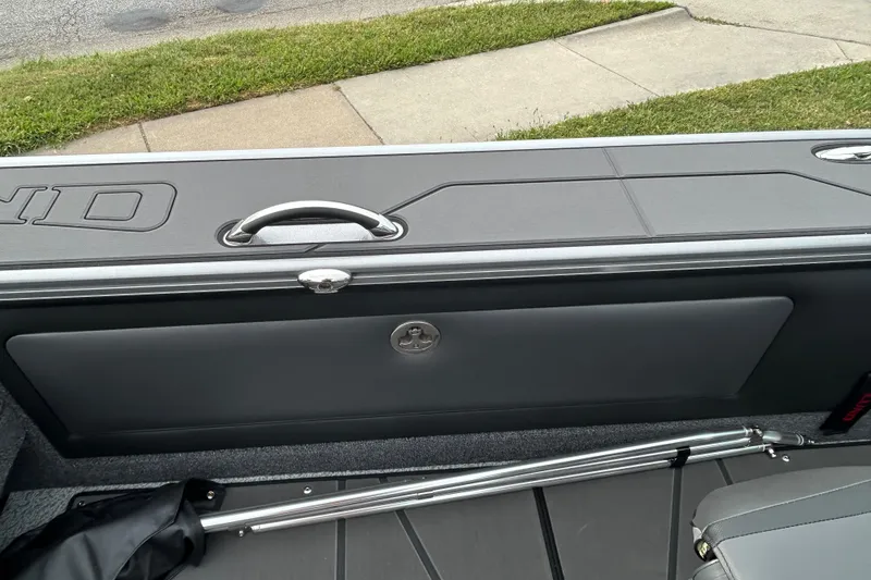 Slide: The Image of 2026 Lund 1875 Pro-V boat interior with storage compartment and handle, parked on grass. - 8