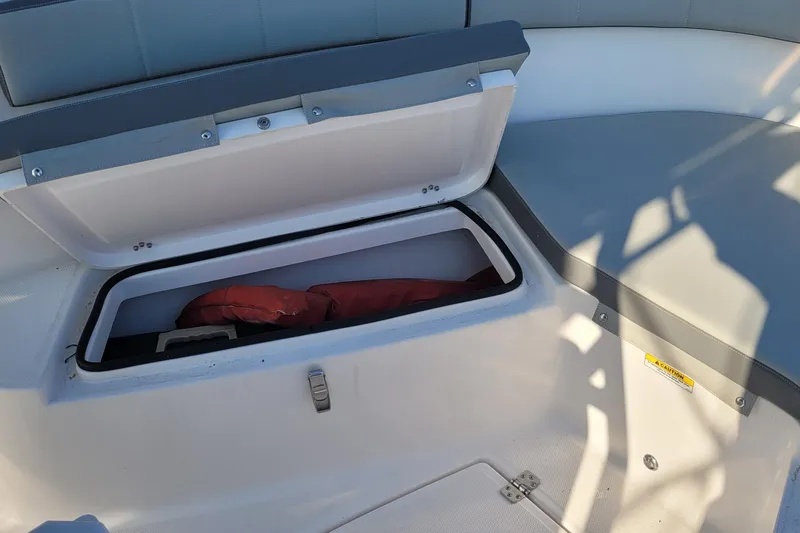 Slide: The Image of 2022 Aquasport 2100 Center Console boat storage compartment with open lid and life jacket inside. - 46