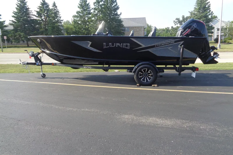 The Image of 2026 Lund 1775 Adventure SS boat on trailer, parked on asphalt near trees. - 1