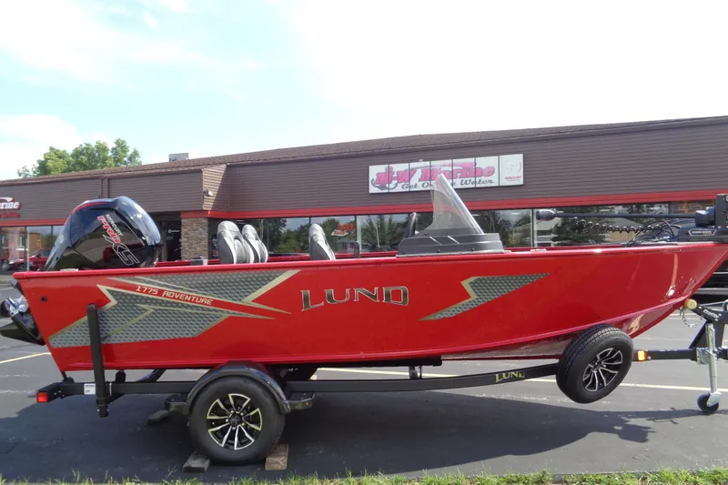 The Image of 2026 Lund 1775 Adventure SS boat in vibrant red on a trailer, parked outside a dealership. - 0