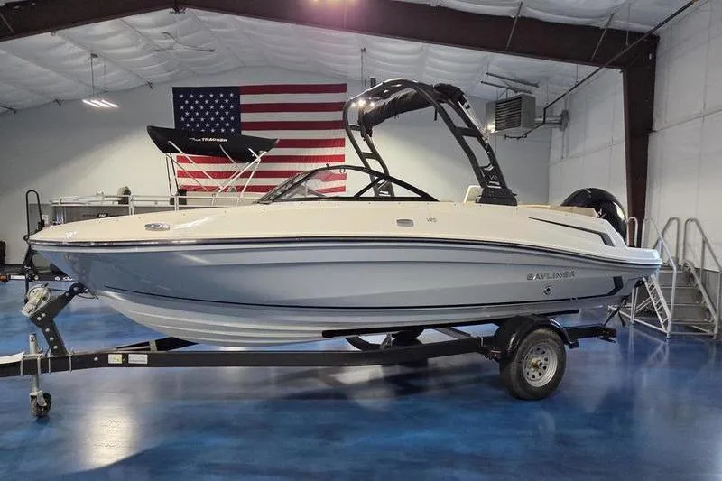 Slide: The Image of 2025 Bayliner VR5 OB boat on trailer in indoor showroom with American flag backdrop. - 5