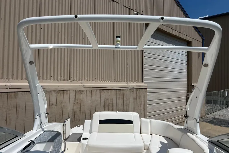 Slide: The Image of 2016 Chaparral 244 Sunesta boat with white seating and arch, parked near a warehouse. - 21