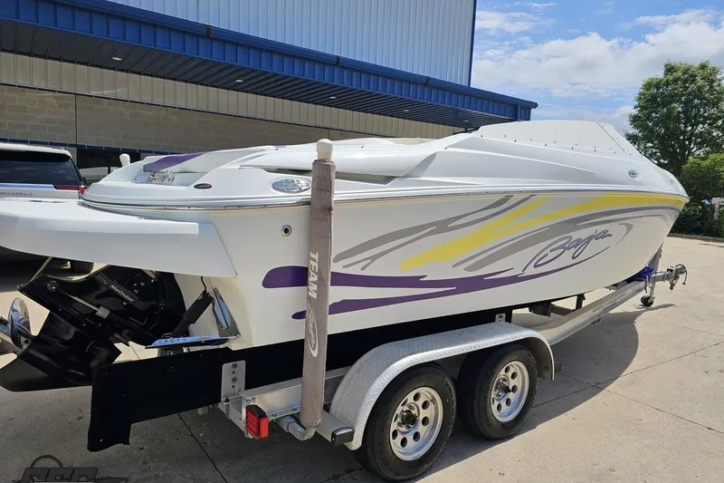 Slide: The Image of 2005 Baja 245 boat on trailer, white with purple and yellow accents, parked outdoors. - 10