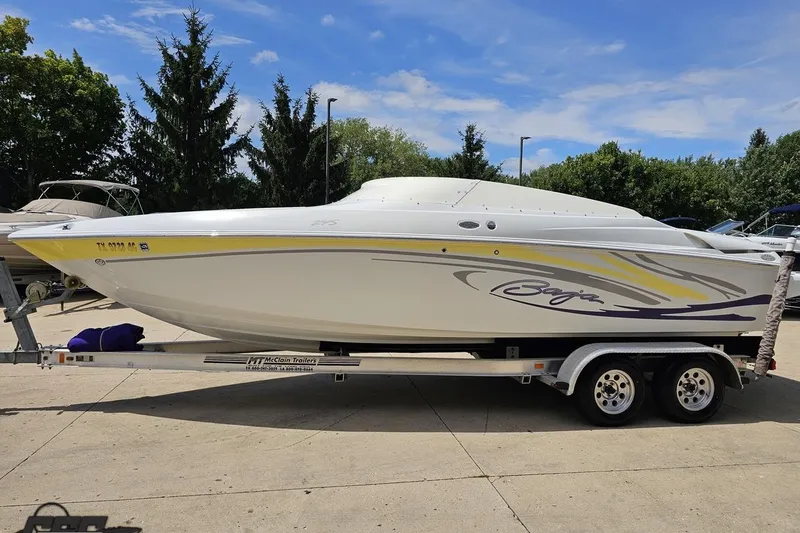 Slide: The Image of 2005 Baja 245 boat on trailer, white with yellow and purple accents, parked outdoors. - 18