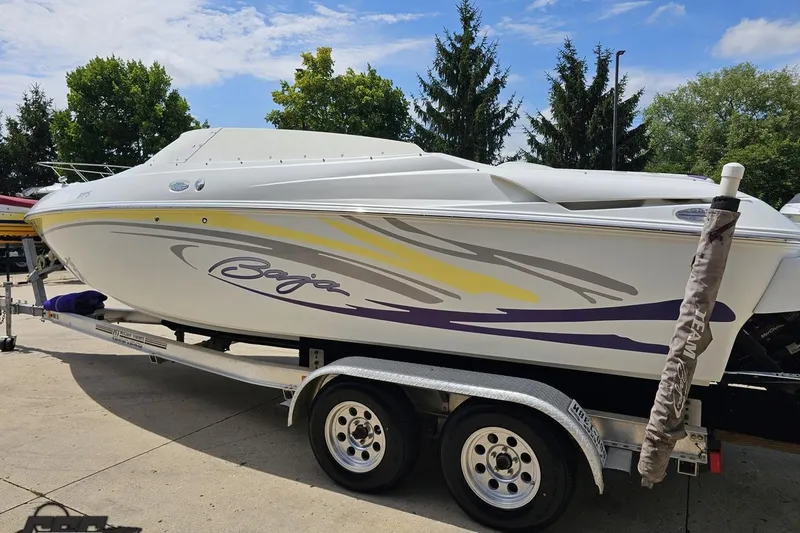 Slide: The Image of 2005 Baja 245 boat on trailer, white with yellow and purple accents, parked outdoors. - 24
