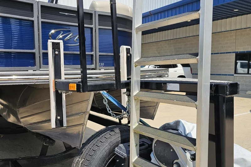 Slide: The Image of 2016 Manitou 23 Legacy boat with ladder and trailer in a parking lot. - 17