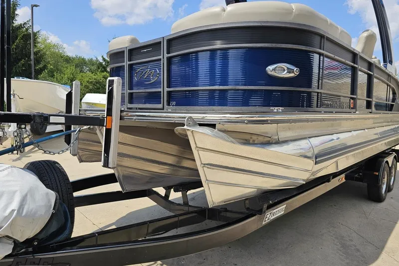 Slide: The Image of 2016 Manitou 23 Legacy pontoon boat on trailer, featuring sleek blue and silver design. - 24