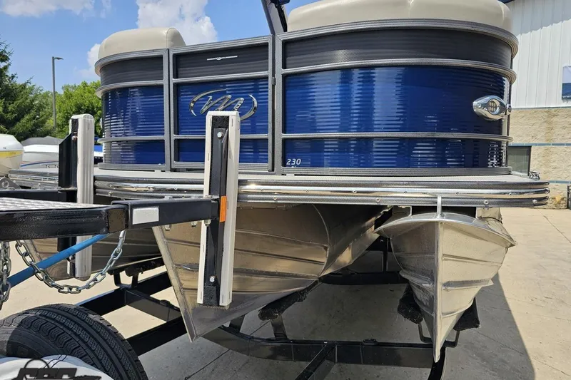 Slide: The Image of 2016 Manitou 23 Legacy pontoon boat on trailer, featuring blue exterior and dual pontoons. - 25