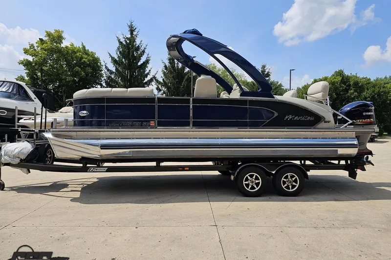Slide: The Image of 2016 Manitou 23 Legacy pontoon boat on trailer, blue and silver design, parked outdoors. - 32