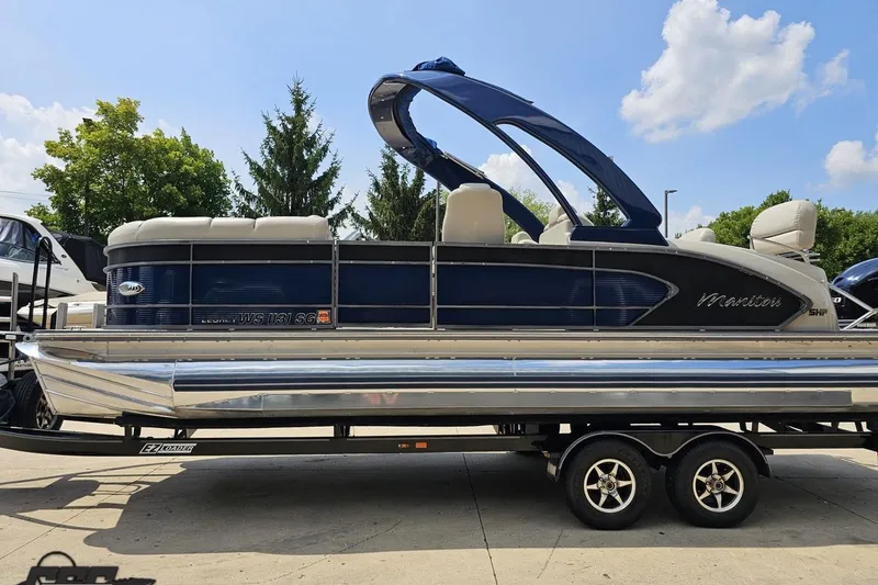 Slide: The Image of 2016 Manitou 23 Legacy pontoon boat on trailer, blue and silver design, sunny day. - 33