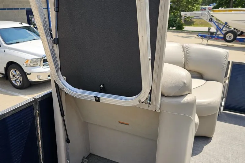 Slide: The Image of 2016 Manitou 23 Legacy pontoon boat interior with beige seating and open storage compartment. - 74