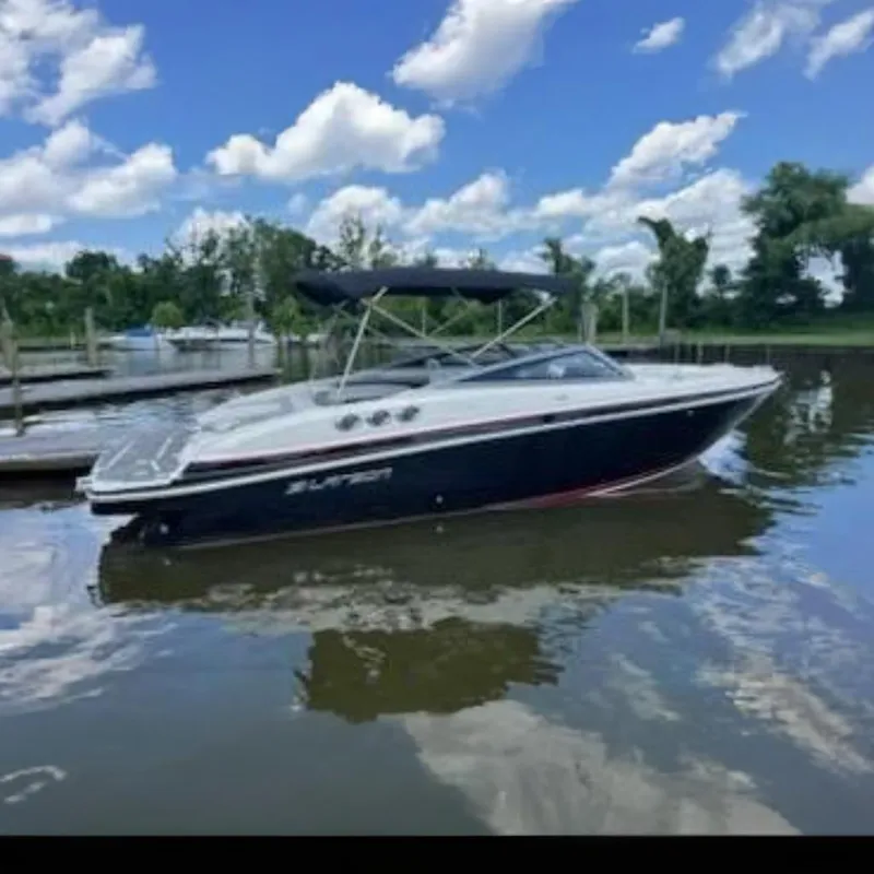 Slide: The Image of 2014 Larson LXi 258 IO boat on calm water, under a partly cloudy sky. - 0
