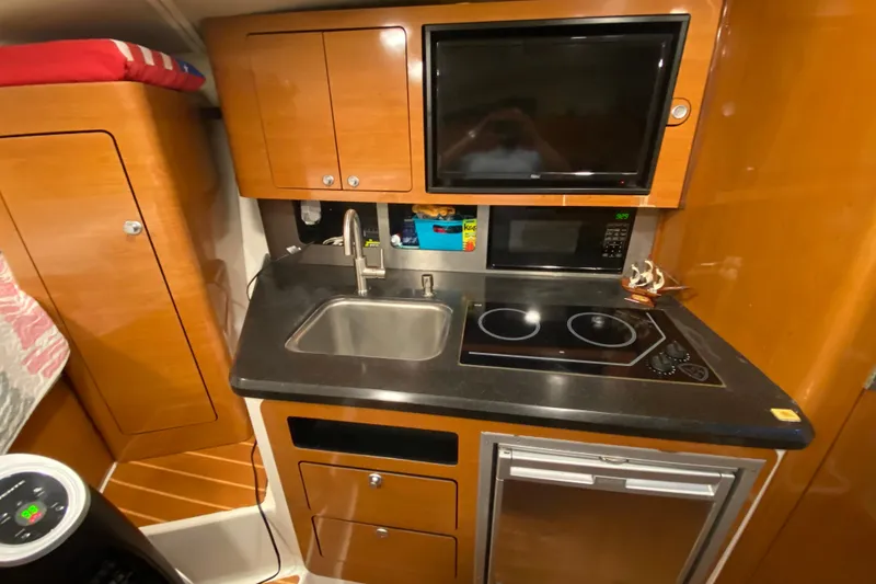 Slide: The Image of 2009 Century 3200 Offshore boat kitchen with sink, stove, microwave, and wooden cabinetry. - 28