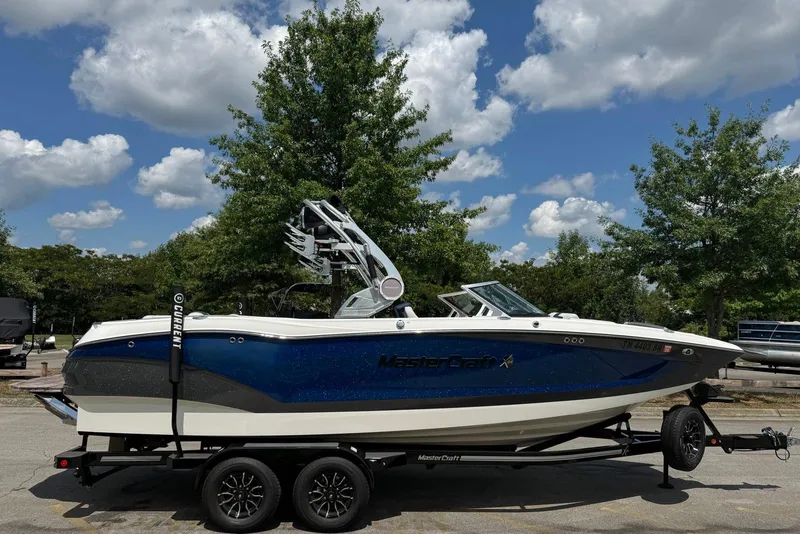 The Image of 2021 MasterCraft X24 boat on trailer under a partly cloudy sky. - 0