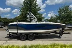 Slide: The Image of 2021 MasterCraft X24 boat on trailer, blue and white, parked outdoors. - 1