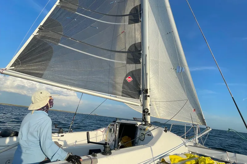 Slide: The Image of Sailor navigating a 2006 Corsair Sprint 750 sailboat on open water under clear skies. - 17