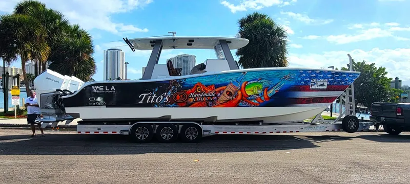 Slide: The Image of 2021 Vela 368 Center Console boat with vibrant graphics on a trailer, parked near palm trees. - 41