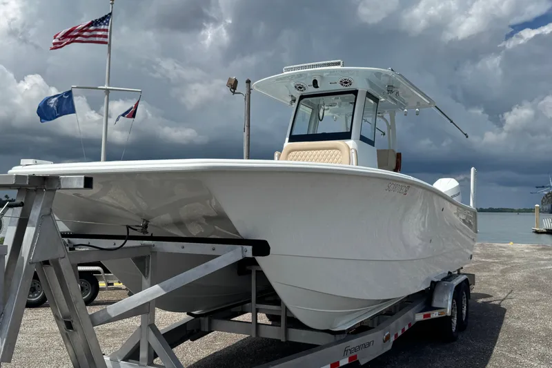 Slide: The Image of 2024 Freeman 28 boat on trailer, dockside with flags and cloudy sky. - 34