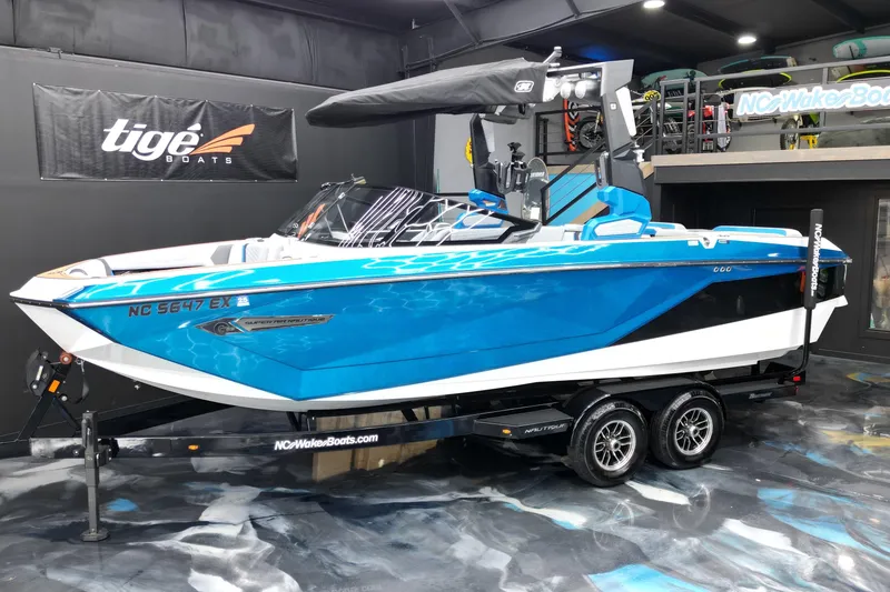 The Image of 2022 Nautique Super Air Nautique G23 boat in showroom, vibrant blue and white design. - 1