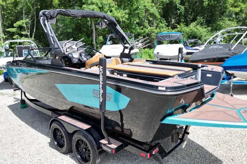 Slide: The Image of 2022 Heyday WTSurf boat on trailer, parked outdoors with lush greenery background. - 11