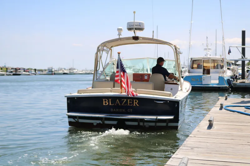 Slide: The Image of 2013 Hunt Harrier boat "Blazer" departing dock, American flag displayed, sunny marina setting. - 38