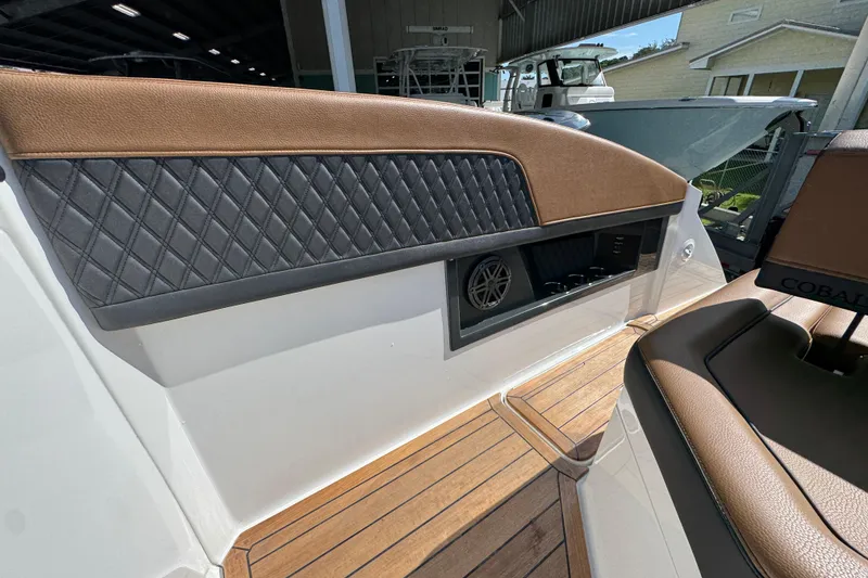 Slide: The Image of 2024 Cobalt R33 boat interior with brown and black leather seating, wood flooring, and speaker system. - 37