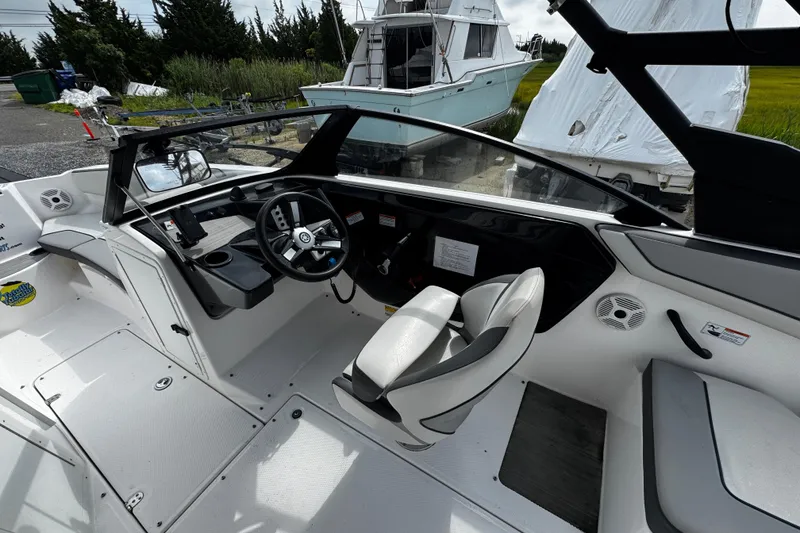Slide: The Image of 2023 Yamaha Boats AR220 interior with steering wheel and seating, docked near other boats. - 9