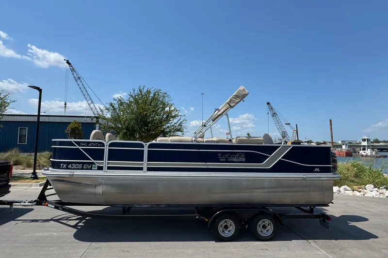 Slide: The Image of 2019 G3 X22FC pontoon boat on trailer, parked near waterfront with cranes in background. - 5