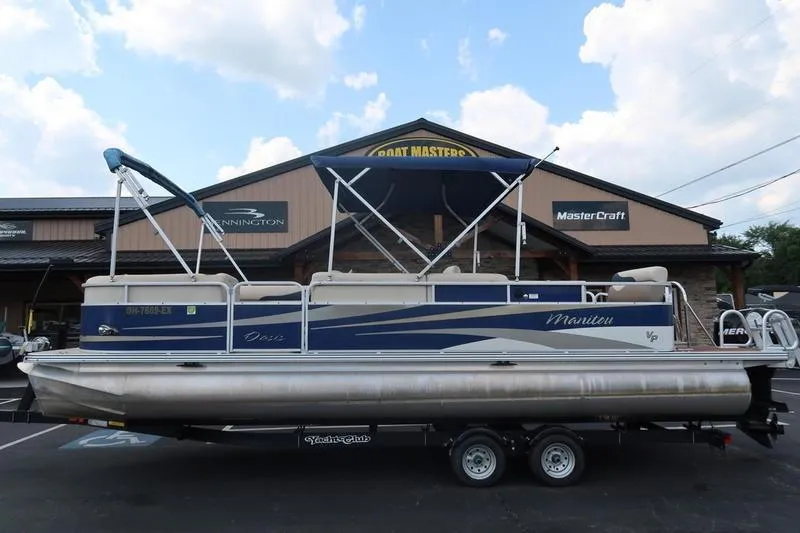 The Image of 2012 Manitou 24 Oasis Tri-Toon pontoon boat on trailer, parked outside dealership. - 1