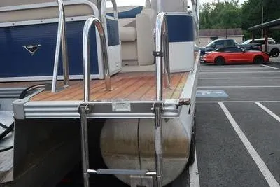 Slide: The Image of 2012 Manitou 24 Oasis Tri-Toon boat with wooden deck and metal railings in parking lot. - 13