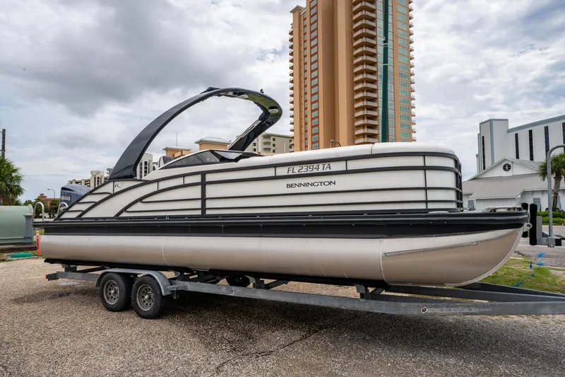 Slide: The Image of 2021 Bennington R25 Sport pontoon boat on trailer, urban background, cloudy sky. - 1