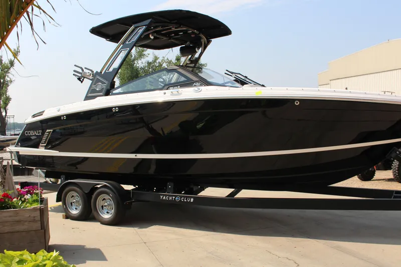 Slide: The Image of 2025 Cobalt R8 Surf boat on trailer, sleek black design, parked outdoors. - 2