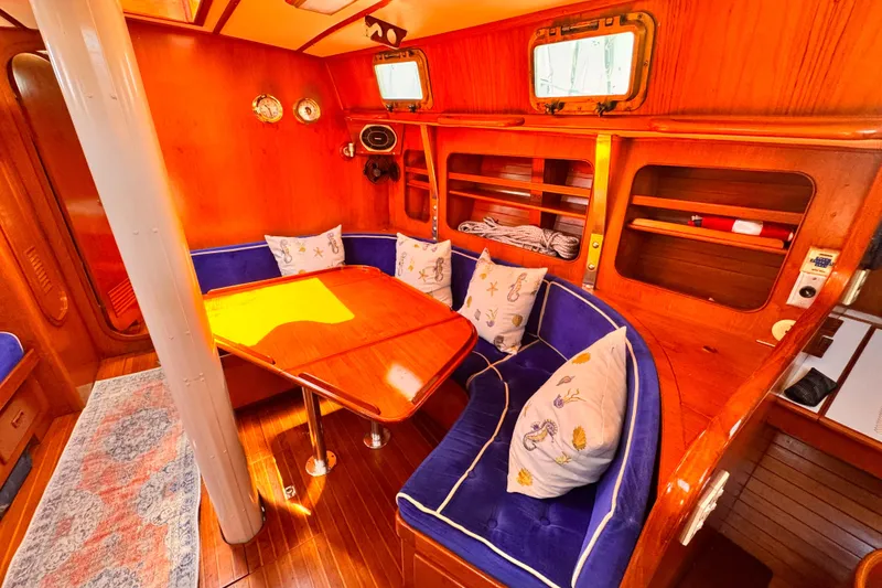 Slide: The Image of Cozy 1982 Kelly Peterson 46 yacht interior with wooden dining area and blue cushioned seating. - 3