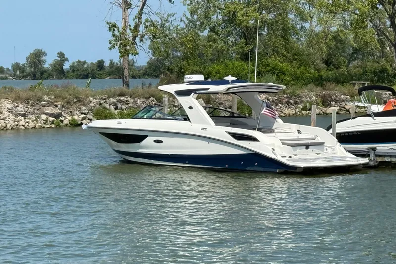 Slide: The Image of 2020 Sea Ray SLX 350 boat docked on a calm lake with trees in the background. - 2