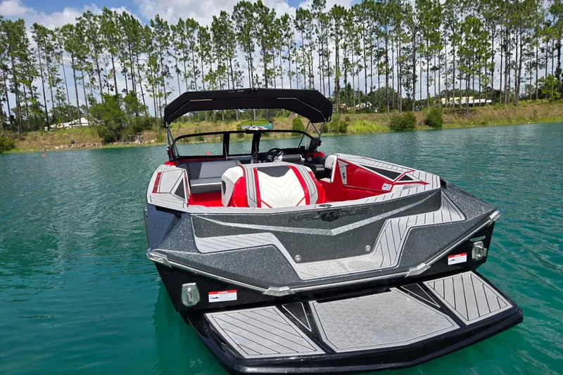 Slide: The Image of 2025 Nautique Ski Nautique boat on a serene lake with lush tree backdrop. - 7