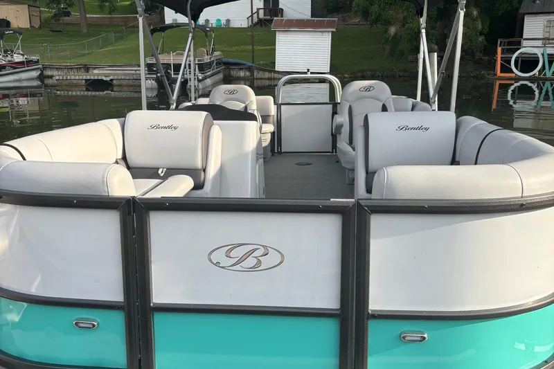 Slide: The Image of 2023 Bentley Pontoons 220 Navigator, luxury pontoon boat with white seating, docked by a lakeside. - 2