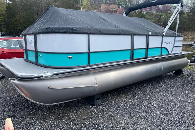 Slide: The Image of 2023 Bentley Pontoons 220 Navigator with cover, parked on gravel, featuring teal and white panels. - 3