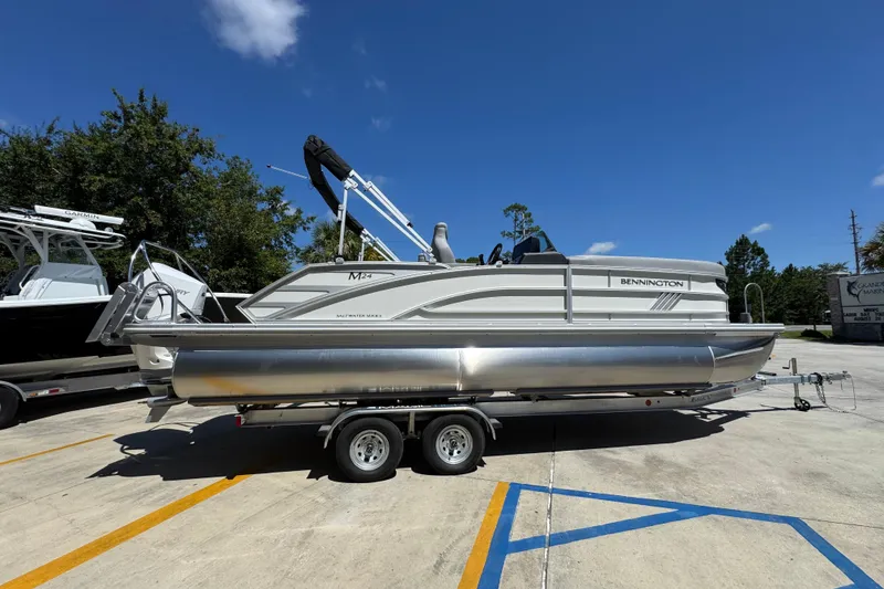 Slide: The Image of 2026 Bennington 24 MSB pontoon boat on trailer, parked outdoors under clear blue sky. - 10
