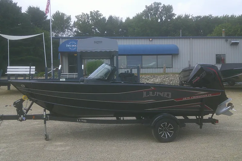 The Image of 2026 Lund 1875 Crossover XS boat on trailer, parked outside a building. - 1