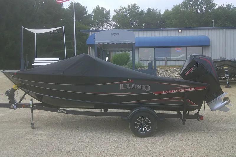Slide: The Image of 2026 Lund 1875 Crossover XS boat with cover on trailer, parked outside dealership. - 17