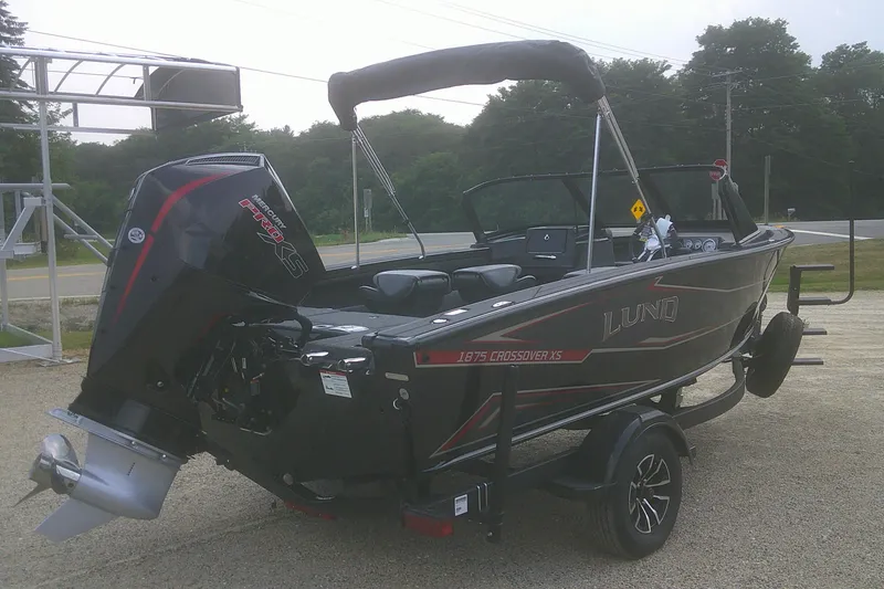 Slide: The Image of 2026 Lund 1875 Crossover XS boat on trailer, featuring a powerful outboard motor. - 2