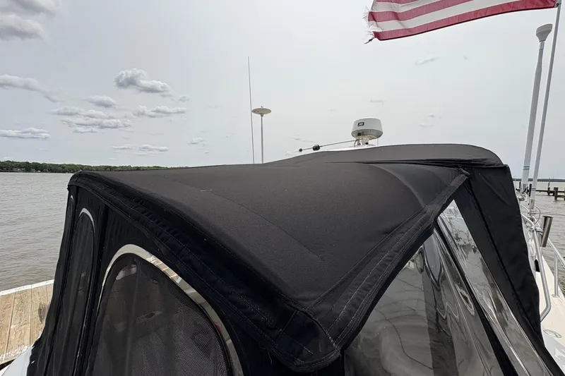 Slide: The Image of 2001 Sea Ray 460 Sundancer with black canopy, docked by a calm lake under cloudy sky. - 12