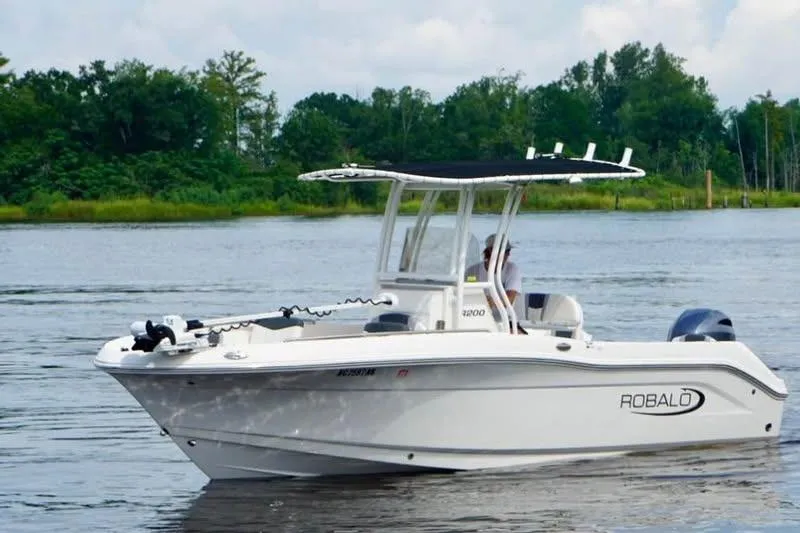 Slide: The Image of 2023 Robalo R200 Center Console boat on a calm lake with lush greenery. - 12