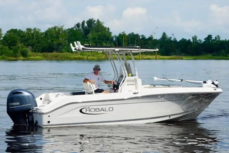 Slide: The Image of 2023 Robalo R200 Center Console boat on a calm lake with lush greenery. - 14