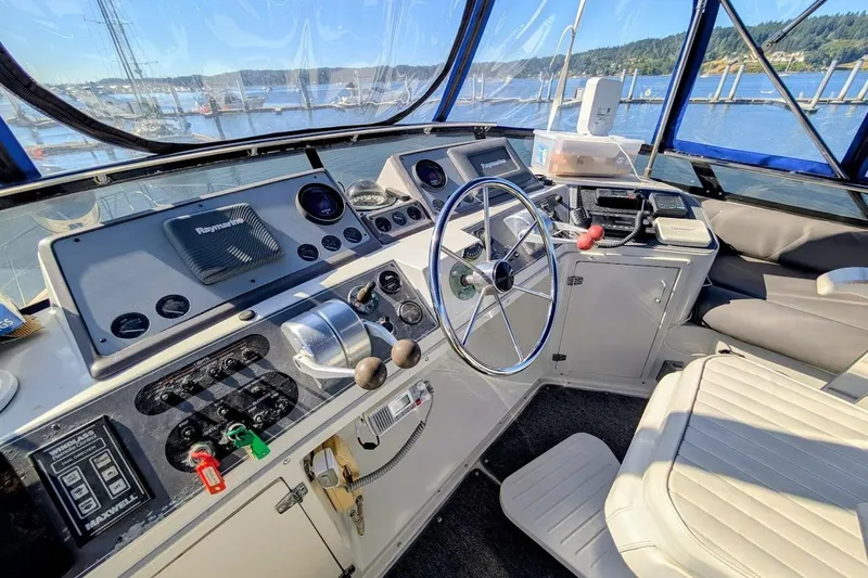 Slide: The Image of 1990 Carver 55 yacht helm with navigation equipment, steering wheel, and marina view. - 35
