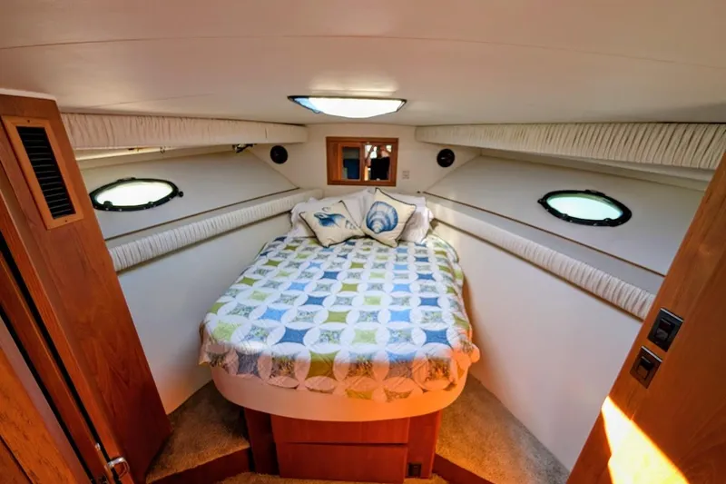 Slide: The Image of 1990 Carver 55 yacht bedroom with cozy bed, decorative pillows, and porthole windows. - 21